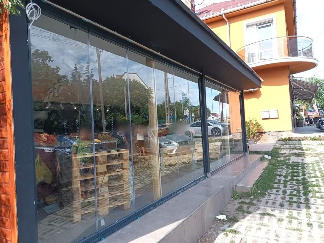 Üzlethomlokzat teljes hosszában lapozható üvegfallal, a táblák egymásra fordítva nyithatók.